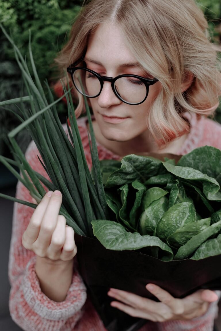 A woman in eyeglasses holds fresh leafy vegetables, showcasing organic produce.