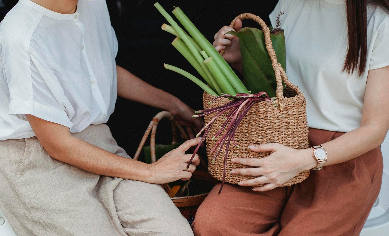 Two women holding wicker baskets filled with fresh vegetables in an outdoor setting, conveying a natural lifestyle.
