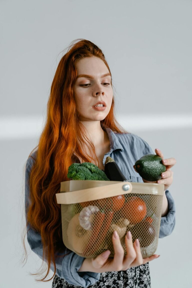 Young woman holding a basket filled with fresh organic vegetables, including avocado and broccoli.