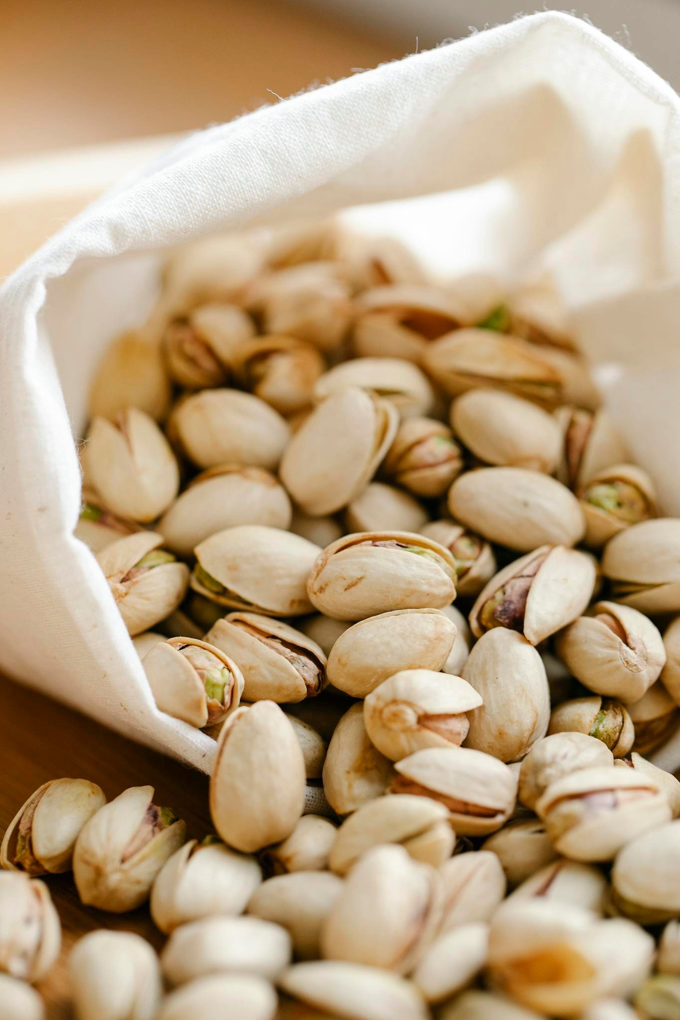 A close-up image of pistachios spilling out of a reusable eco bag on a table.
