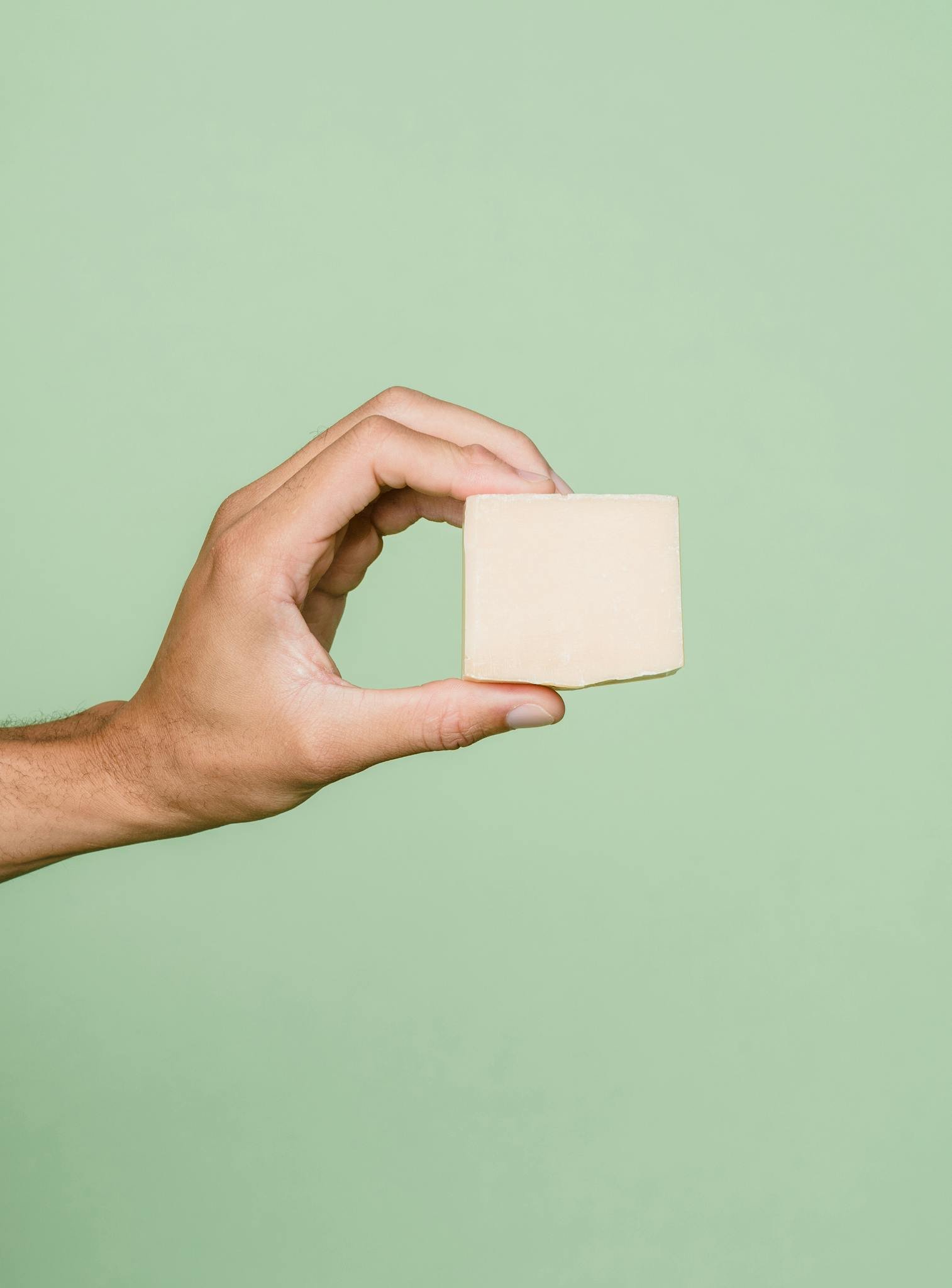 A human hand holding a tofu block against a minimalist green background, showcasing healthy vegan food.