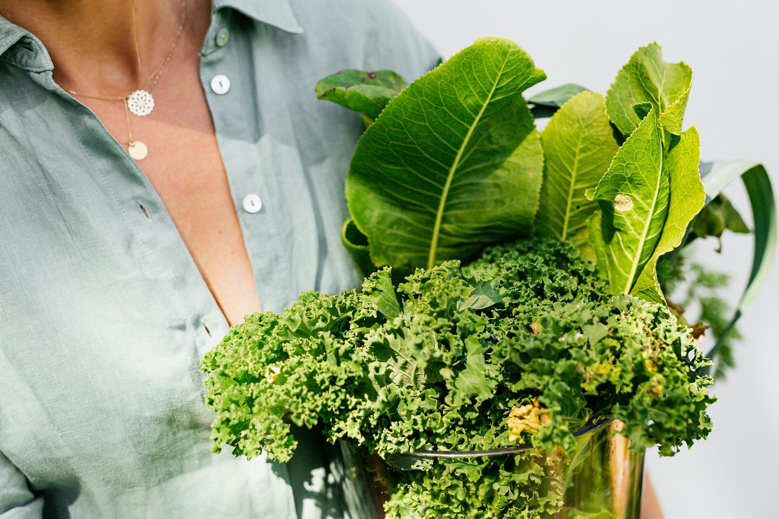 Close-up of fresh curly kale and leafy greens held by woman in green shirt.